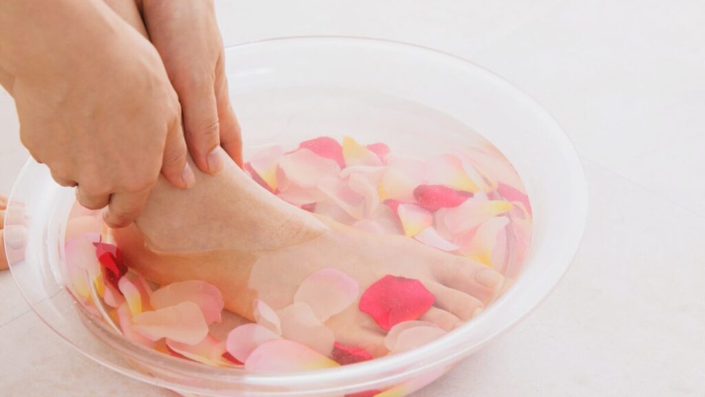 バラの花びらを浮かべた洗面器に見右足をつけて両手でさすっているさすっている女性